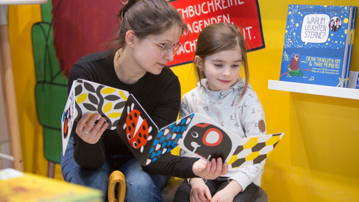 Frau und Mädchen lesen gemeinsam ein Bilderbuch auf der Leipziger Buchmesse 2024