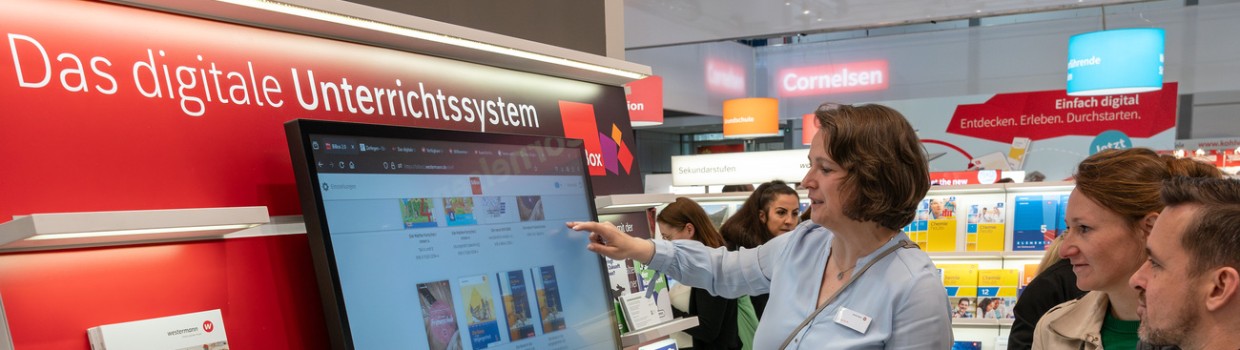 Frau demonstriert Besucher:innen das digitale Unterrichtssystem an einem Bildschirm auf der Leipziger Buchmesse 2024