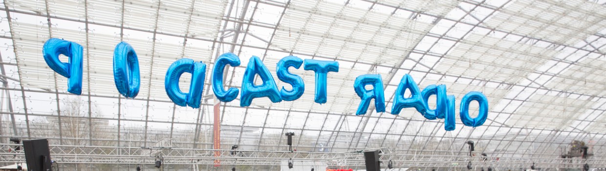 Auf der Lesebühne von detektor.fm findet eine Lesung vor Publikum in der Glashalle während der Leipziger Buchmesse 2024 statt. Darüber schweben blaue Luftballons mit dem Schriftzug "Podcast Radio".